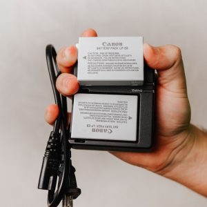 Close-up of a hand holding a Canon battery charger with cables, essential for photography electronics.