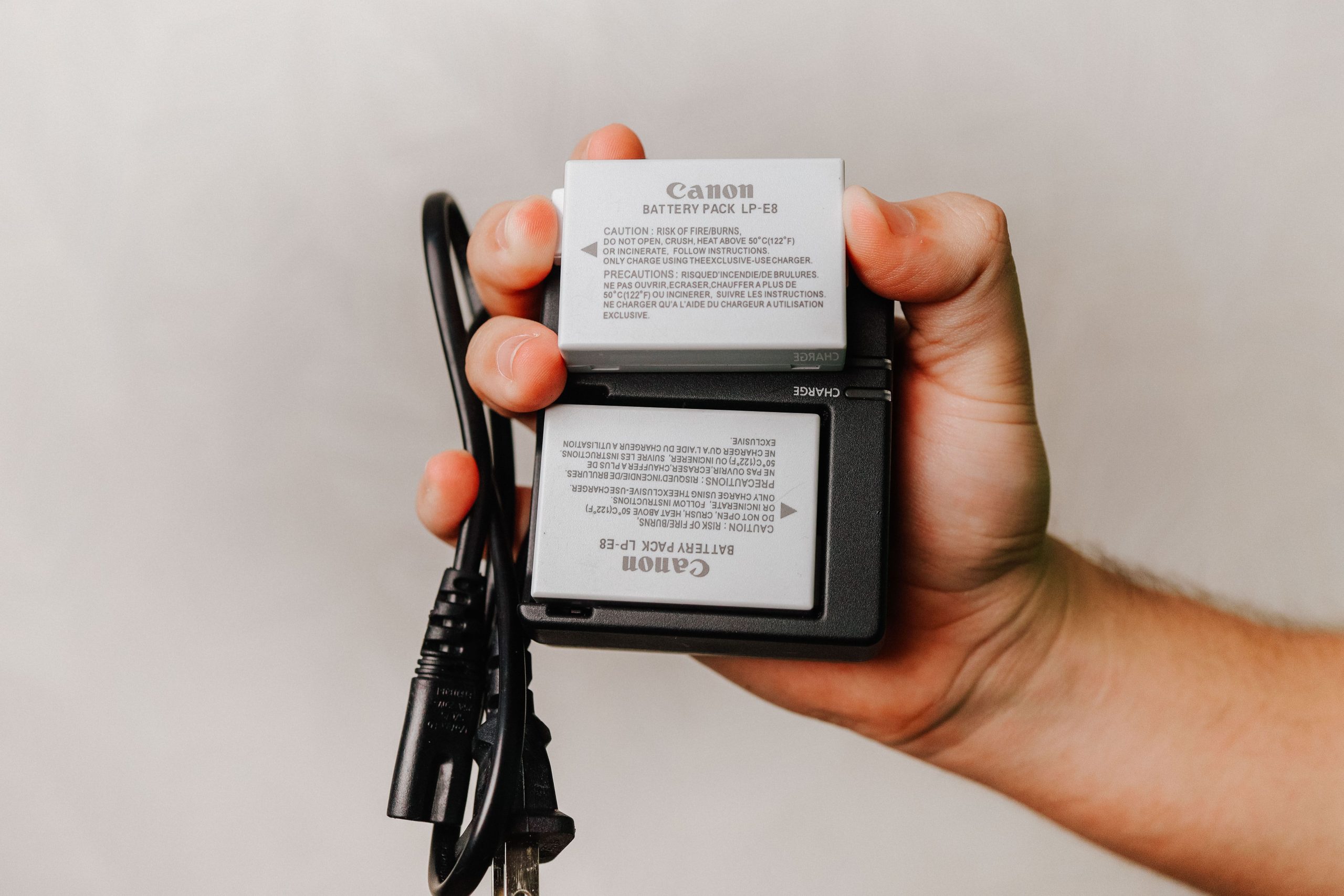 pexels photo 10668297 10668297 Close-up of a hand holding a Canon battery charger with cables, essential for photography electronics.