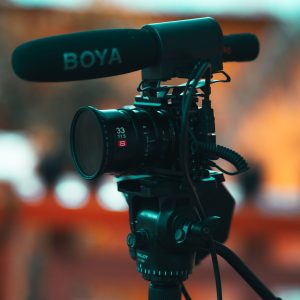 Close-up of a professional video camera mounted on a tripod with a microphone outdoors.