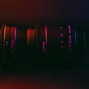 Moody close-up of Canon 24mm and 18-55mm lenses under vibrant lighting.