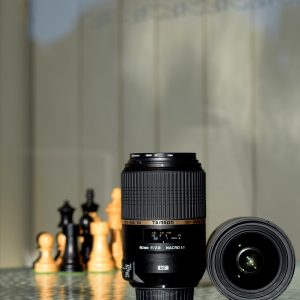 Photography lens and chess pieces placed on a reflective surface illustrating focus and strategy.