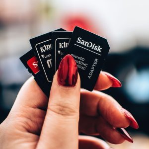 A close-up image of a woman's hand holding multiple microSD memory cards with red nails.