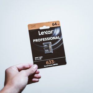 A hand holding a packaged 64GB Lexar Professional SD card, ideal for digital storage.