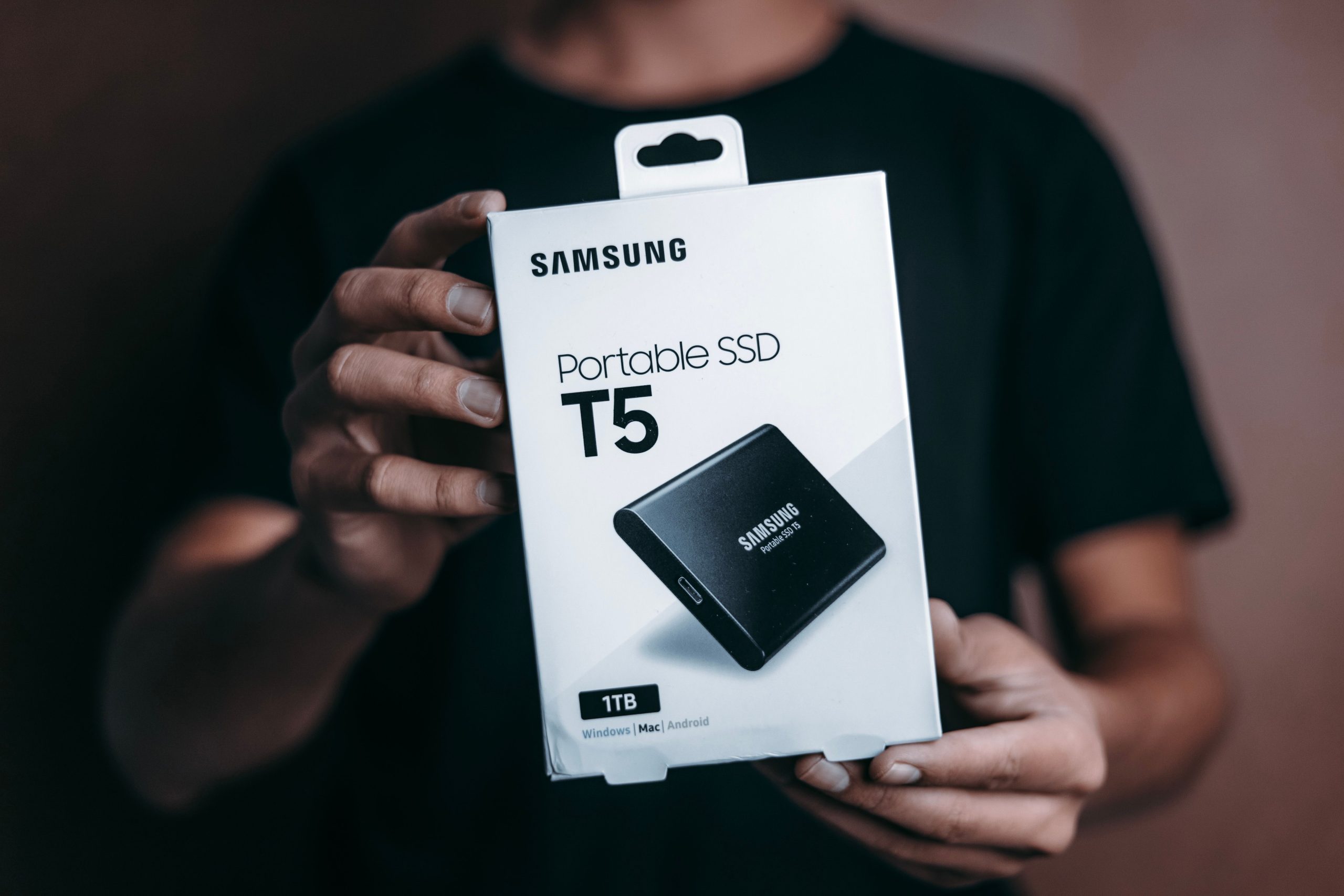 pexels photo 2942361 2942361 Close-up of a person holding a Samsung T5 Portable SSD box, emphasizing modern technology.