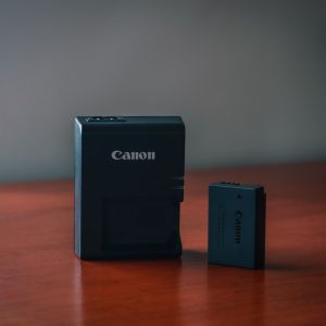 Close-up of a Canon battery and charger on a wooden table with a blurred background.
